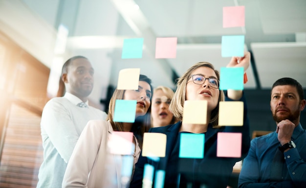 Creative group or business team planning for innovation with sticky notes on glass wall Coach or leader sharing vision and mission in a meeting Manager sharing ideas and explaining strategy