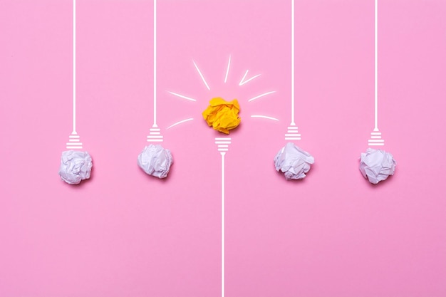 Creative idea of crumpled paper A burning light bulb on a pink background