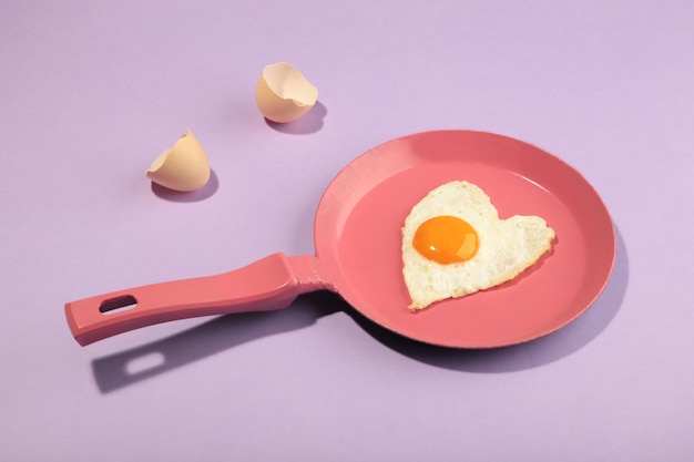 Creative idea with a pink frying pan and egg in heart shape on white and pink background Minimal food and love concept Breakfast idea for Valentine's day and romantic morning Top view