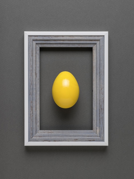 Creative image of a bright yellow egg in a frame on a gray background. Flat lay.