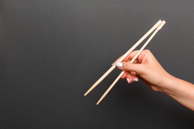 Creative image of wooden chopsticks in female hand on black . Japanese and chinese food with copyspace