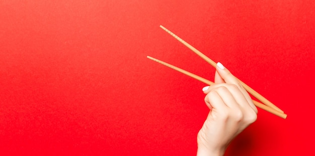 Creative image of wooden chopsticks in female hand on red