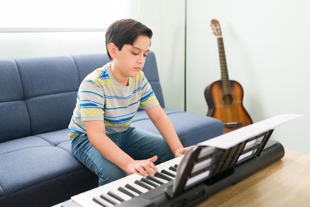 Creative kid playing the piano at home and practicing for his music lessons. Artistic boy learning to play a new musical instrument