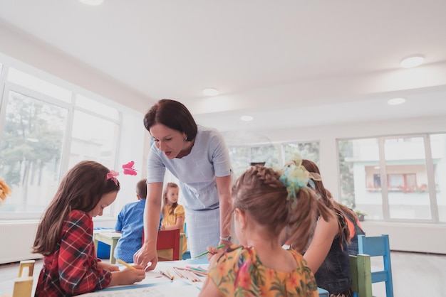 creative kids during an art class in a daycare center or elementary school classroom drawing with female teacher