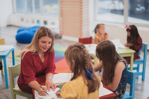 Creative kids during an art class in a daycare center or elementary school classroom drawing with female teacher