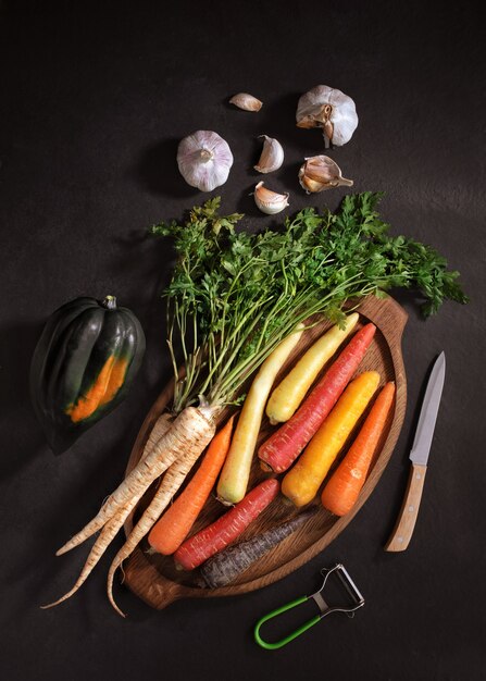 creative lay out of carrots, eggplant, radish and garlic on wooden cutting board on black background