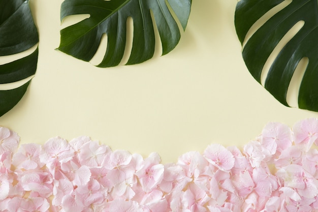 Creative layout and background made of tropical palm leaves and pink pastel flowers. Summer concept on yellow backdrop. Flat lay, top view, copy space.