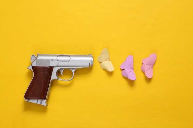 Foto layout creativo di pistola e farfalle su sfondo giallo nessuna guerra vista dall'alto