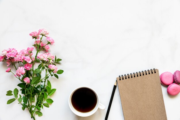 Photo creative layout made of pink rose flowers bouquet, coffee cup, blank notebook and macaroons