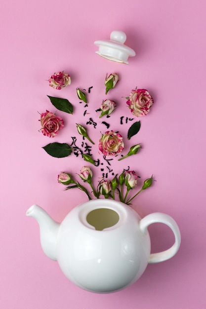 Foto layout creativo con fiori che volano fuori dalla teiera. bollitore e rose. sfondo rosa. vista dall'alto. disposizione piatta. concetto di ora del tè.