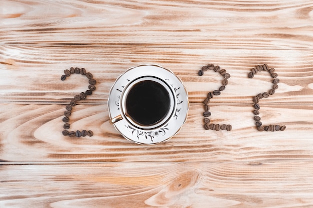 사진 나무 배경에 있는 커피 콩과 컵으로 만든 창의적인 글자 2022입니다. 크리스마스와 새해 커피 컨셉