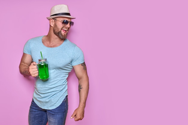 Creative male in sunglasses and summer clothes stylish hat standing relaxed and drinking from creati...