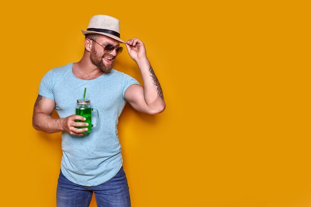 Creative male in sunglasses and summer clothes stylish hat standing relaxed and drinking from creati...