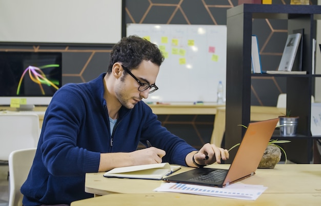 Creative man making notes at hisworkplace in bright modern office