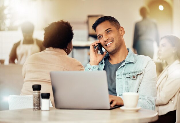 Creative man phone and laptop at cafe with smile for communication networking or conversation Happy male freelancer smiling for call discussion or startup on smartphone at coffee shop restaurant