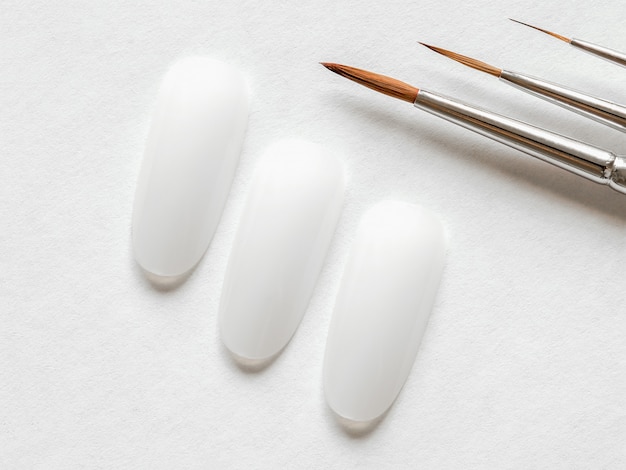 Creative manicure concept. Clean tips and paint brushes of different sizes for manicure on a white wall