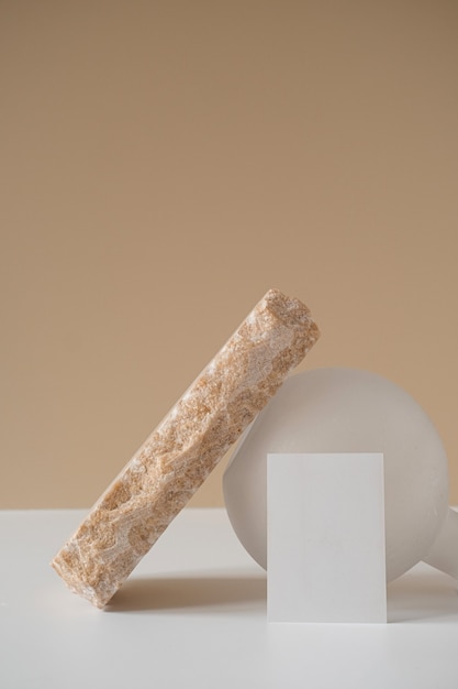 Креативная минималистичная эстетическая концепция с пустым листом бумаги, розовым мраморным камнем, белой вазой на нейтральной бежевой стене.