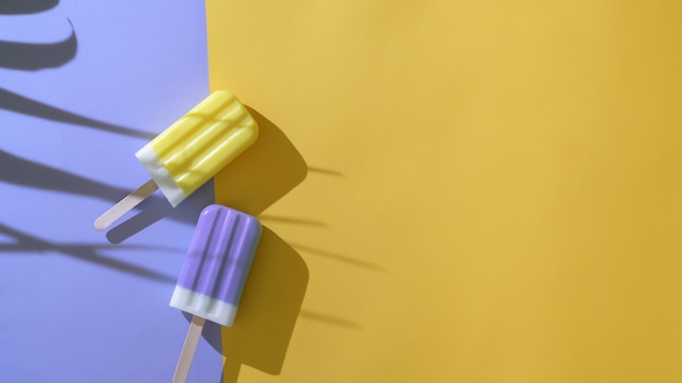 Creative minimal summer concept, top view of two colourful popsicles on purple and  yellow background