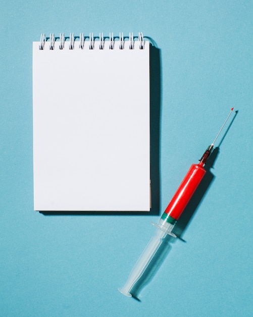 Creative minimalistic concept with a red syringe on a blue background with space for text. Vaccine and medicine