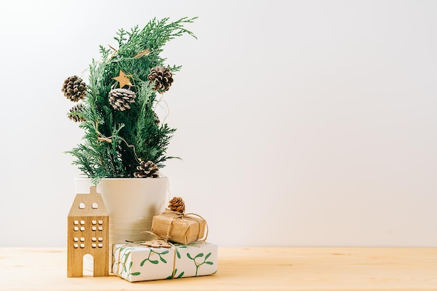 Creative natural miniature christmas tree in pot on wooden table with gift boxes and white