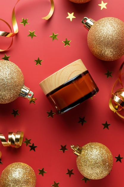 Presentazione creativa di capodanno e natale di packaging cosmetico barattolo di crema senza marchio in vetro ambrato con coriandoli di palline d'oro glitterate su sfondo rosso mockup alla moda per il tuo marchio