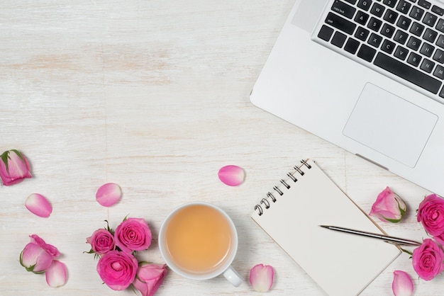 Creative office desktop with roses with a blank paper sheet laptop and cup of aromatic tea on pink