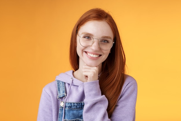 Creative outgoing young charismatic redhead female coworker discuss casual staff smiling laughing happily have pleasant conversation look camera amused tender touch chin, orange background.