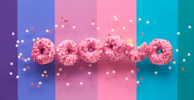 Creative panoramic image of flying tasty pink donuts, one already half eaten. Conceptual levitation of sweet delicious dooughnuts on layered multicolored paper background.