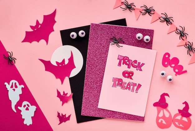 Creative paper craft Halloween flat lay wall in dark red. Top view with bats, ghosts, chocolate eyes, pumpkins, text "Trick or treat" on cards and paper word "Boo".