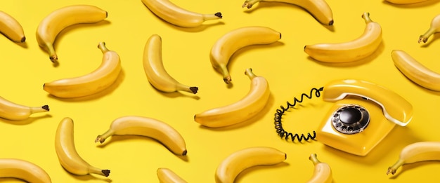 Photo creative pattern bananas and old yellow phone with hard shadows pattern on yellow background flat lay banana phone horizontal banner