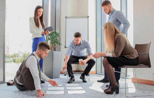 Creative people looking at project plan laid out on floor Business associates discussing project plan in modern office