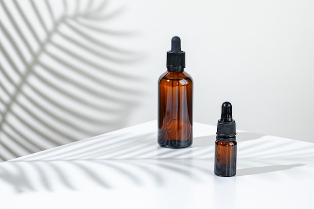 Creative photo of cosmetic bottle with pipette on a white background with shadow of tropical flower. Advertising