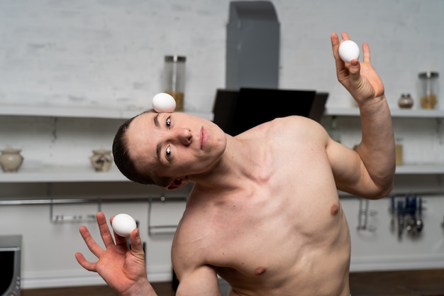 Foto creativa dell'uomo muscoloso in cucina a cucinare le uova.