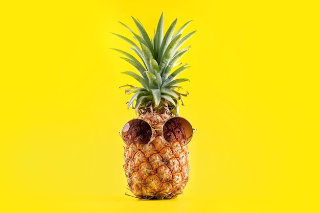 Creative pineapple looking up with sunglasses and shell isolated on yellow background, copy space close up