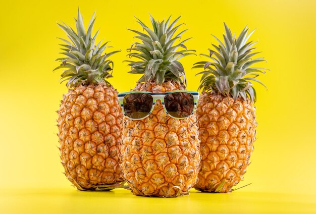 Creative pineapple looking up with sunglasses and shell isolated on yellow background summer vacation beach idea design pattern copy space close up