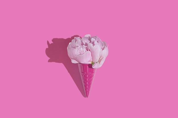 Creative pink toy ice cream cone with pink peony fluffy flower on pink minimal background with copy space flat lay Botany idea for summer or spring wallpaper or greeting card