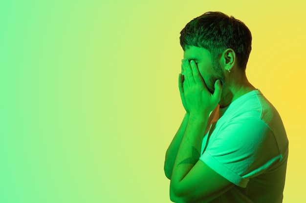 Creative portrait of a bearded middleaged man Depressed man with mental problems Covers her face with her hands and cries Colored green light on yellow backgroundConcept midlife crisis Copy space