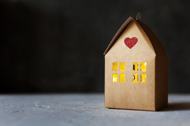Creative present box, cardboard house with lights inside and red heart as symbol of love and happiness
