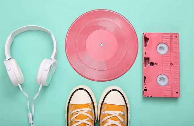 Creative retro 80s layout Pink vinyl record video cassette stereo headphones and sneakers on mint blue background Minimalism Flat lay Top view