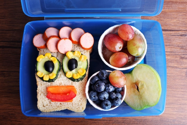 Creative sandwich with fruits in lunchbox on wooden background