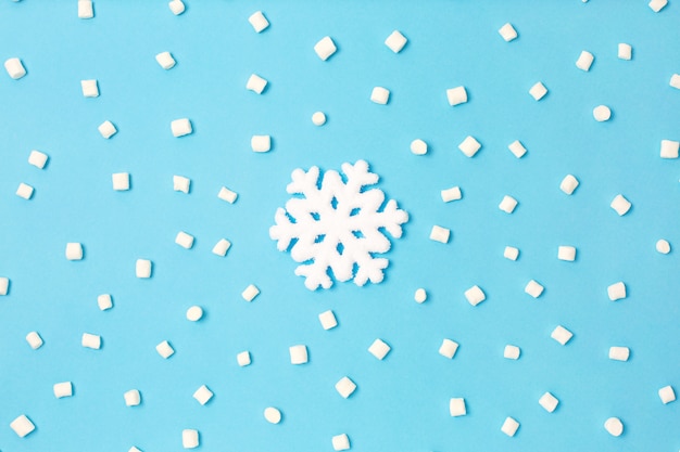 Creative snowlake under white marshmallow on light blue background.