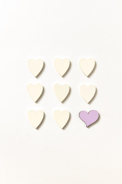 Creative square pattern from small paper handmade white hearts and one of them is pink on a lght grey wall with soft shadows, copy space. Valentine's  Top view.