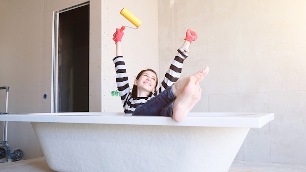 Творческая история молодая счастливая женщина сидит в ванной посреди комнаты с роликом в руках.