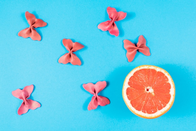 Creative summer layout made of grapefruit and colored pasta semolina papillon on blue background.