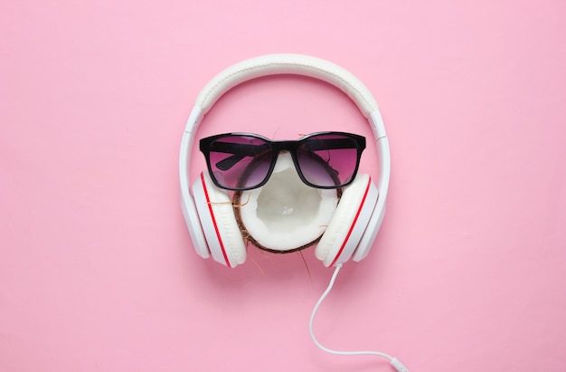 Креативный летний минимализм. кокос, солнцезащитные очки, наушники на розовом пастельном фоне. Вид сверху
