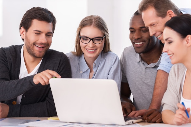 Creative team at work. Group of business people in casual wear sitting together at the table and discussing something while looking at the laptop