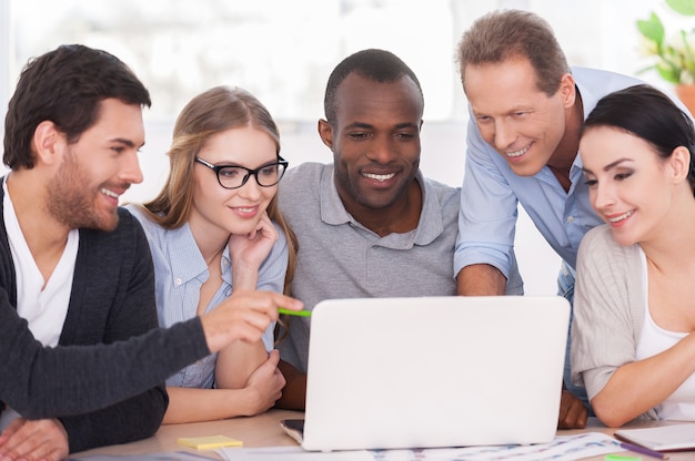 Creative team working on project. Group of business people in casual wear sitting together at the table and looking at the laptop