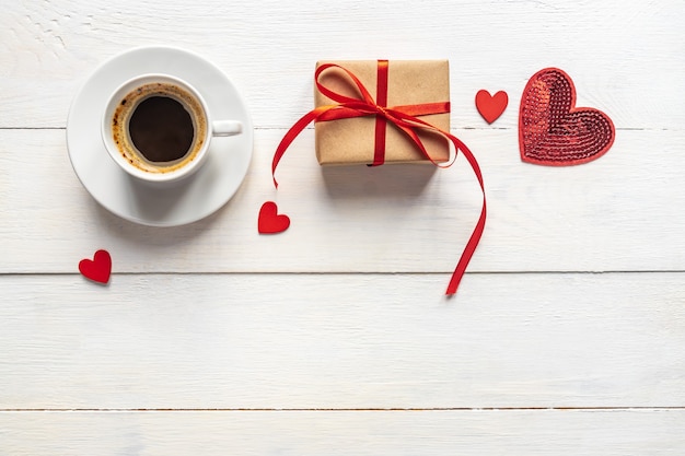 Creative Top view flat lay romantic composition. Hot espresso coffee mug with red gift hearts and craft present box. Concept or birthday or valentines holiday with copy space.