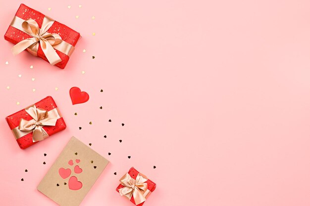 Creative Valentine's Day greeting card with red decorations and gift boxes, golden heart confetti on pink background, copy space, top view