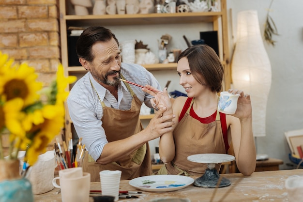 Creative wife. Bearded dark-haired handsome potter coming to workshop of his creative appealing wife